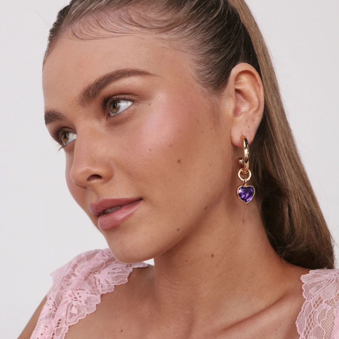 Model wearing a gold hoop with a purple heart charm